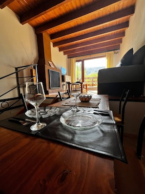 Een eetgedeelte met een houten tafel gedekt voor twee personen, een televisie en uitzicht op het omliggende landschap.