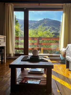 A room with a wooden table, a view of mountains through a glass door, and a wooden deck outside. - VF Catedral Mountain Division (San Carlos de Bariloche)