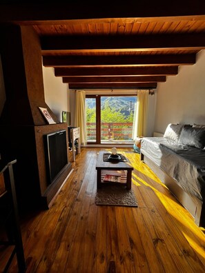 A room with a wooden floor, a sofa, a television, and a window with a view of greenery. - VF Catedral Mountain Division (San Carlos de Bariloche)