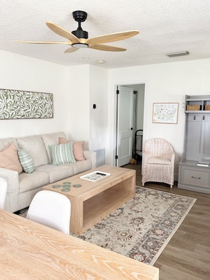 A living room with a sofa, coffee table, and a ceiling fan. - The Cottage On Lime is a 1948 cozy cottage in downtown Sarasota! (Sarasota)