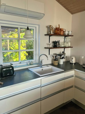 A kitchen with a window, a sink, a toaster, and shelves with kitchenware. - Idyll and charm with views over the fjord (Kalundborg)