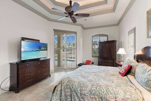 Ein Schlafzimmer mit einem Bett, einem Fernseher auf einer Kommode, einem Deckenventilator und Blick ins Freie durch ein Fenster.