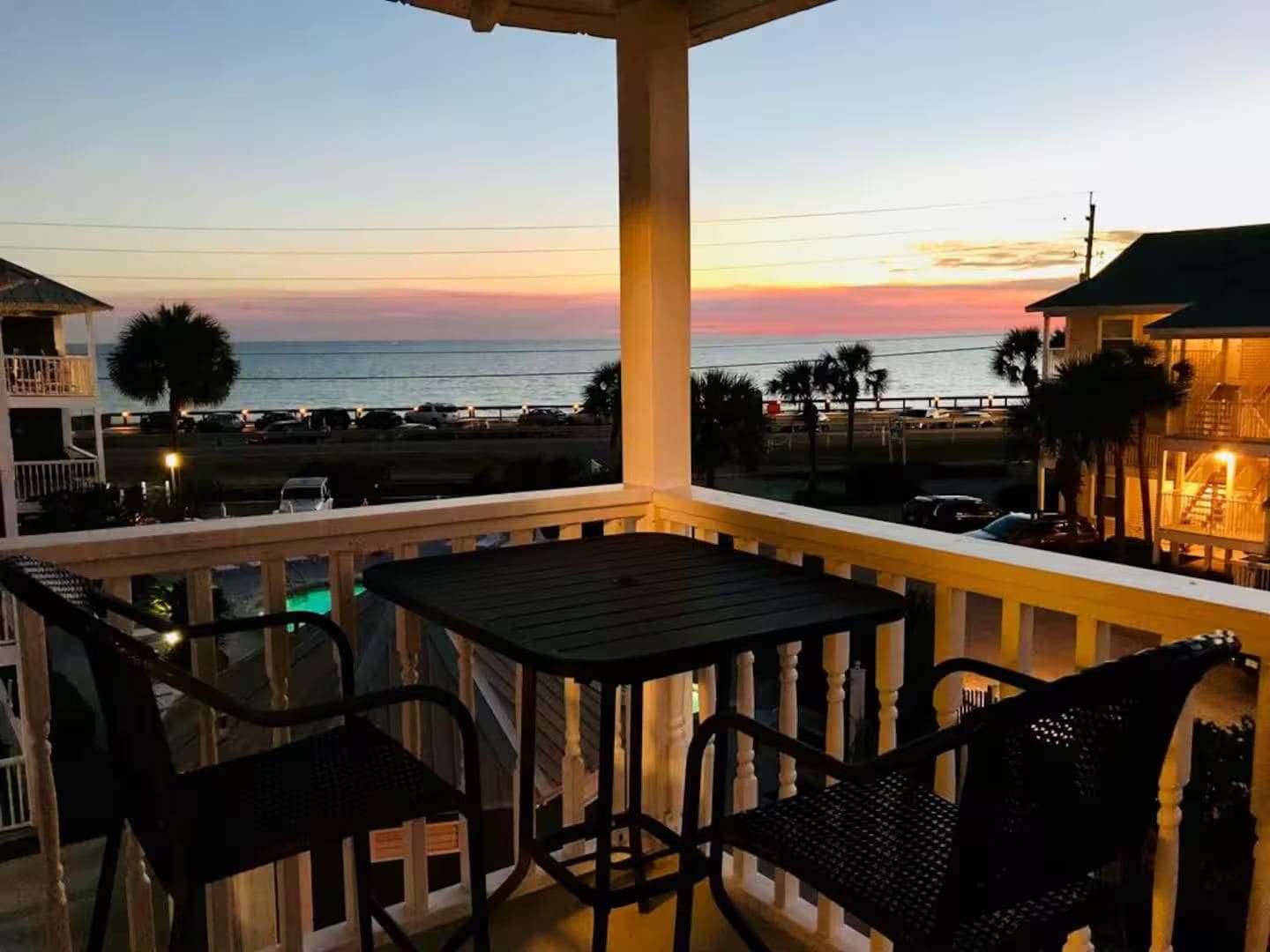 A balcony with a view of the ocean at sunset, featuring a table and two chairs.