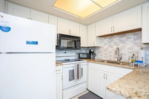 A kitchen with white cabinets, a microwave, a stove, and a sink. - Summer Breeze 310 (Miramar Beach)