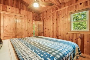 A wooden cabin bedroom with a bed, a window, and a ceiling fan. - Riverside Cabin, Mtn Views, Fire Pit and Fireplace (West Jefferson)