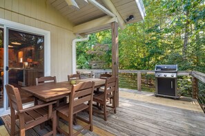 An outdoor deck with a wooden table and chairs, a grill, and a view of a wooded area. - Riverside Cabin, Mtn Views, Fire Pit and Fireplace (West Jefferson)