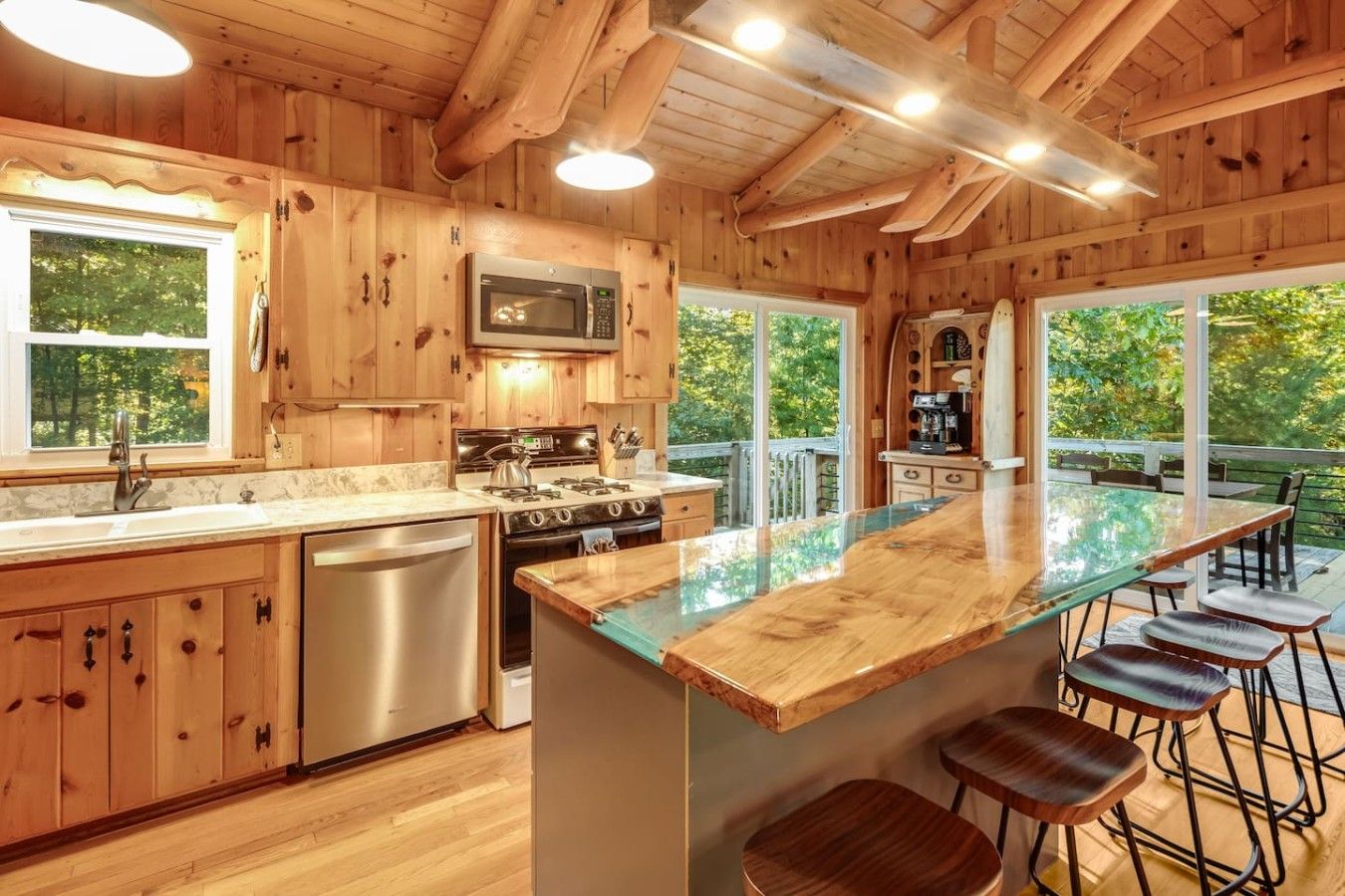 Cocina de cabaña de madera con una isla central, electrodomésticos de acero inoxidable y ventanas grandes.