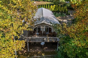 A house with a covered patio area, a fenced yard, and trees with autumn foliage. - Riverside Cabin, Mtn Views, Fire Pit and Fireplace (West Jefferson)