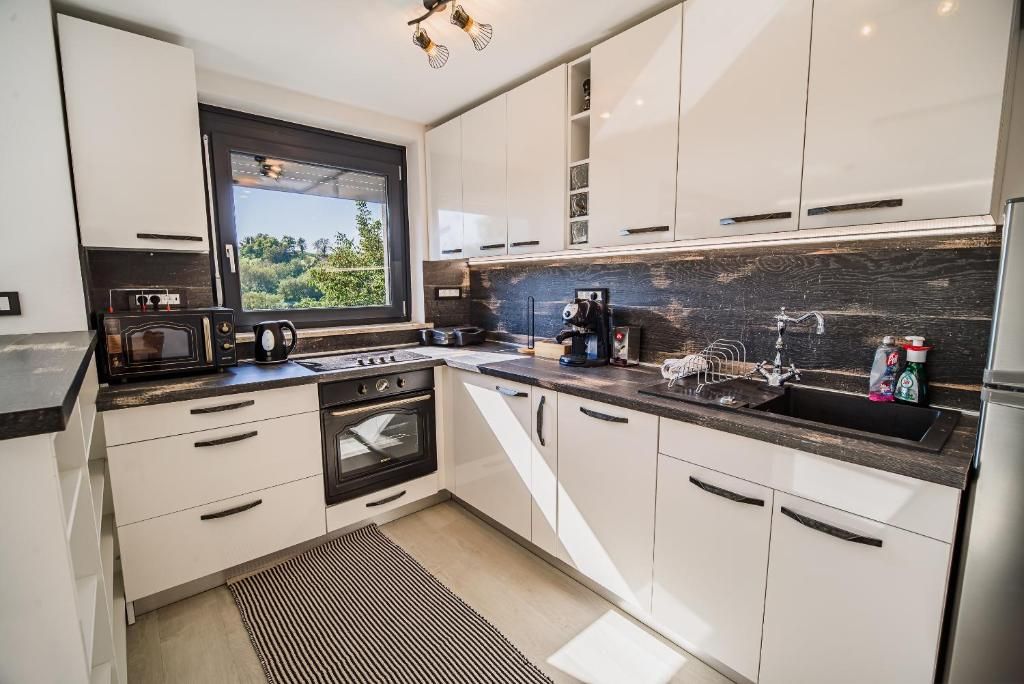 A modern kitchen with white cabinets, a black countertop, a built-in oven, and a window overlooking greenery.
