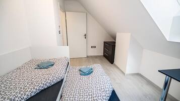 A small, modern room with two beds, a desk, and a wardrobe.