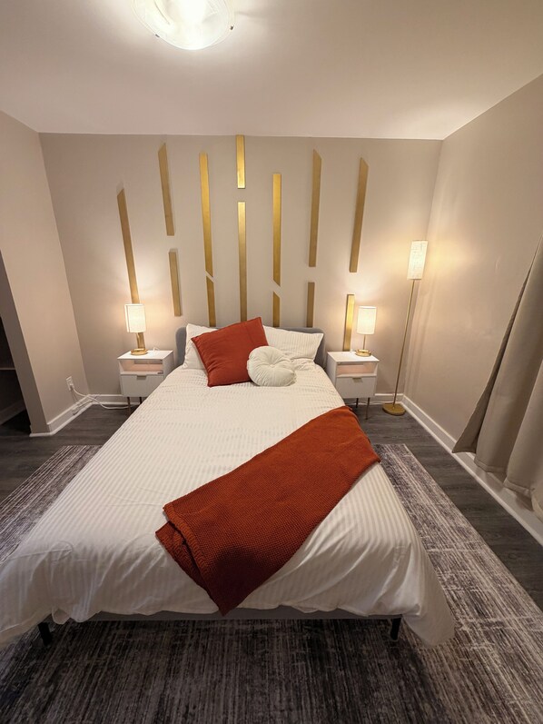 Una camera d'albergo ordinata con un letto grande, due comodini, una lampada da terra e un punto luce a parete.