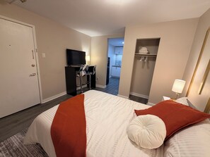 Una camera d'albergo con un letto, una scrivania, una televisione, un armadio e un bagno sullo sfondo.