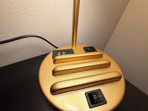A gold-colored, modern lamp with a switch and power outlet on a black surface. - Stylish Studio in St Boniface: French Quarter - cafés, museums, bus route, park (Winnipeg)