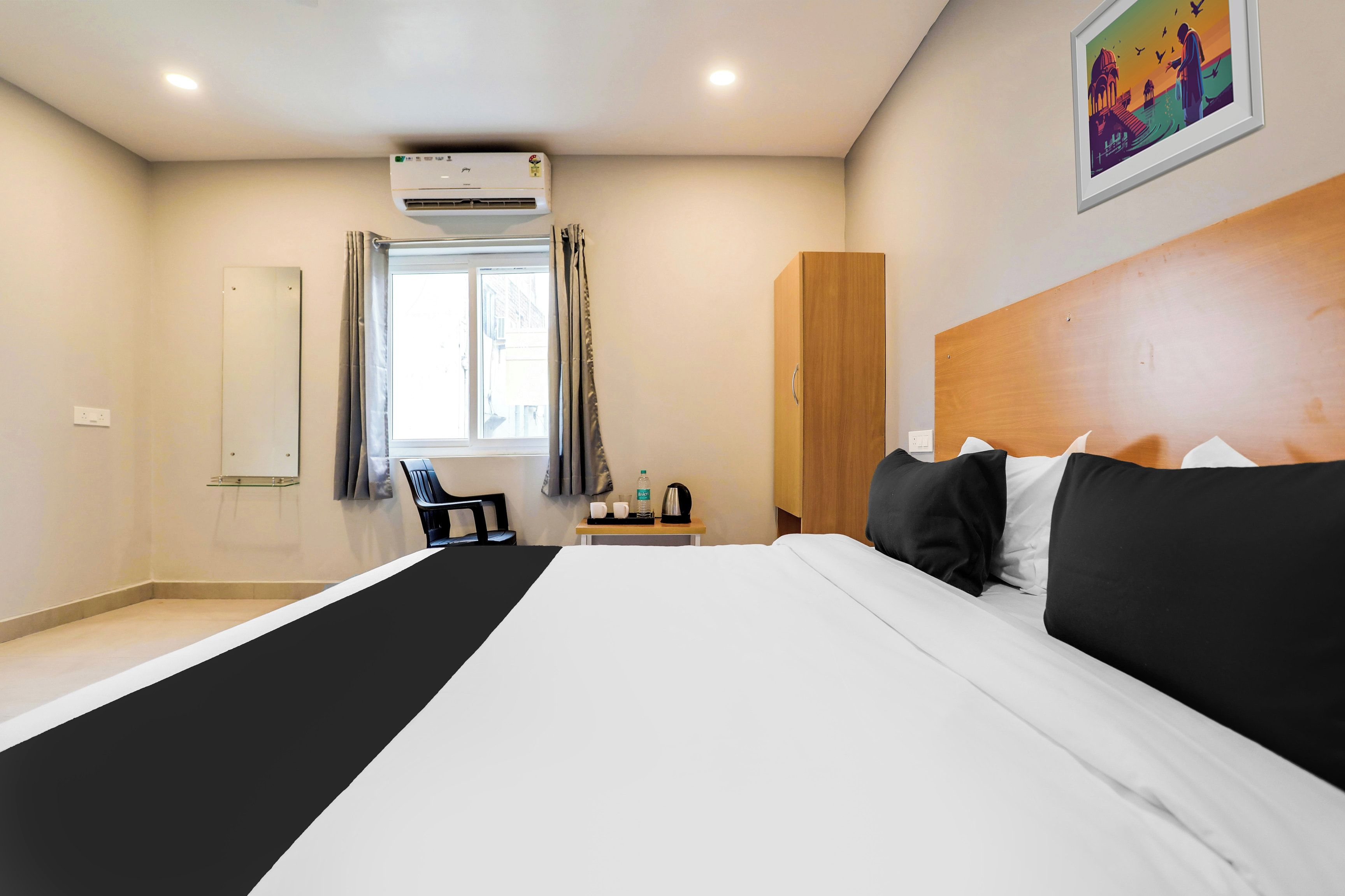 Habitación de hotel con una cama grande, un armario de madera, un escritorio con silla, una ventana con cortinas y un equipo de aire acondicionado.