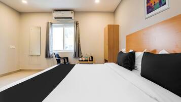 Habitación de hotel con una cama grande, un armario de madera, un escritorio con silla, una ventana con cortinas y un equipo de aire acondicionado.