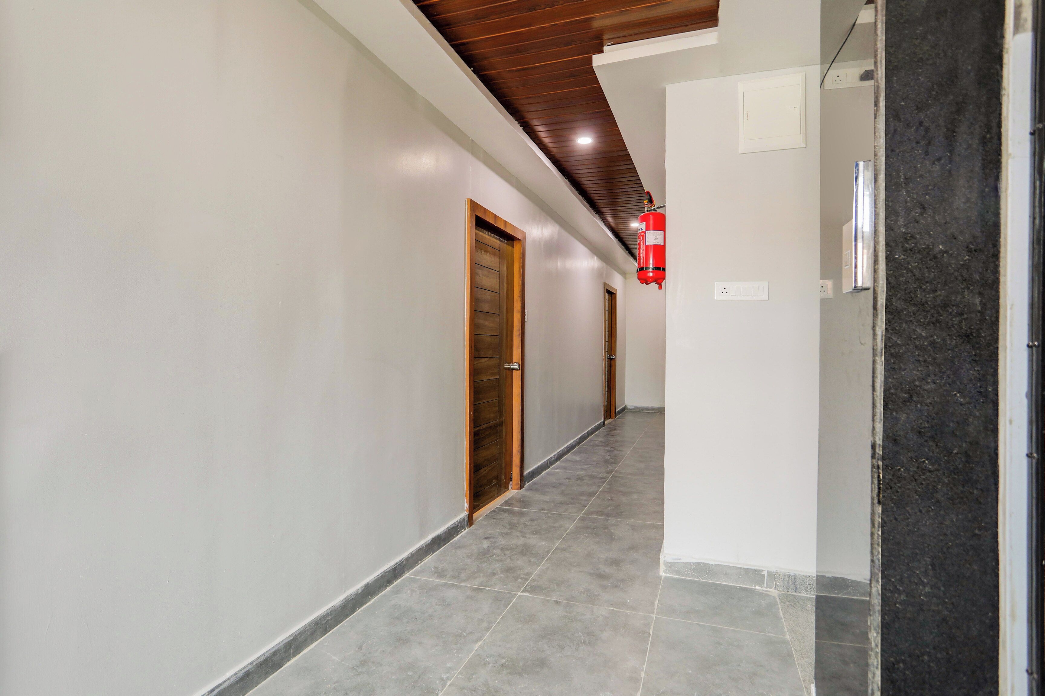 Un pasillo con una puerta de madera, un extintor y un interruptor de luz en la pared.
