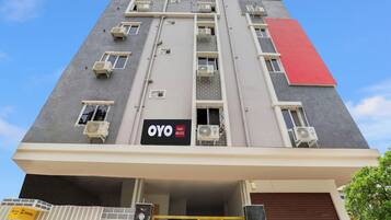 A multi-story hotel building with air conditioning units on each floor, a prominent red section on the facade, and a sign indicating it is an OYO Hotel RBS ECIL.