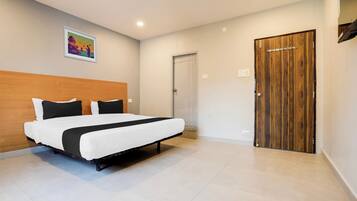 A modern bedroom with a large bed, a wooden headboard, a door with a coat rack, and a ceiling light.
