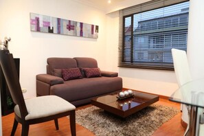 A modern living room with a brown sofa, a glass coffee table, and a painting on the wall. - Hotel Suites 108 (Bogotá)