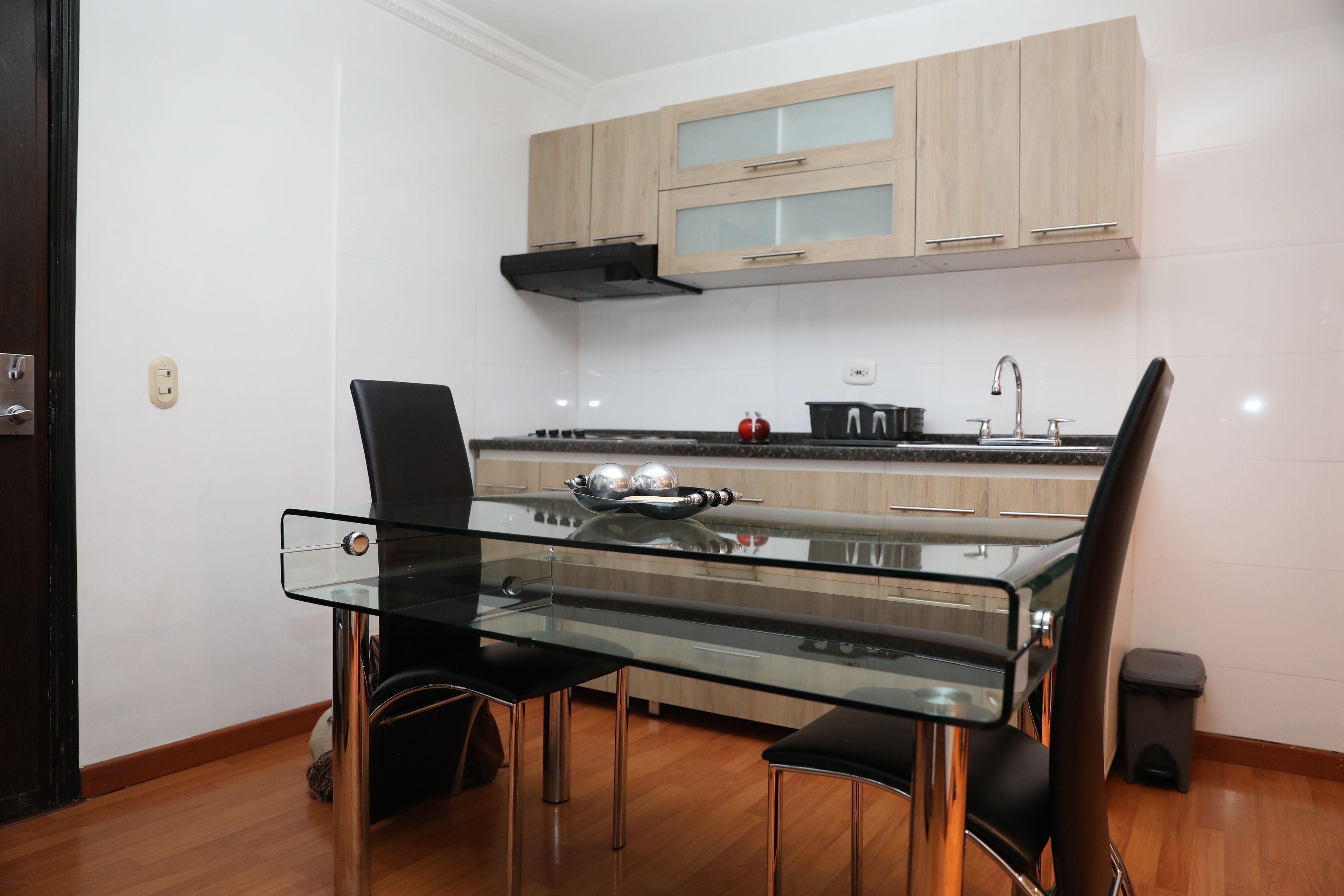 Cozinha moderna com mesa de vidro, cadeiras pretas e armários de madeira.