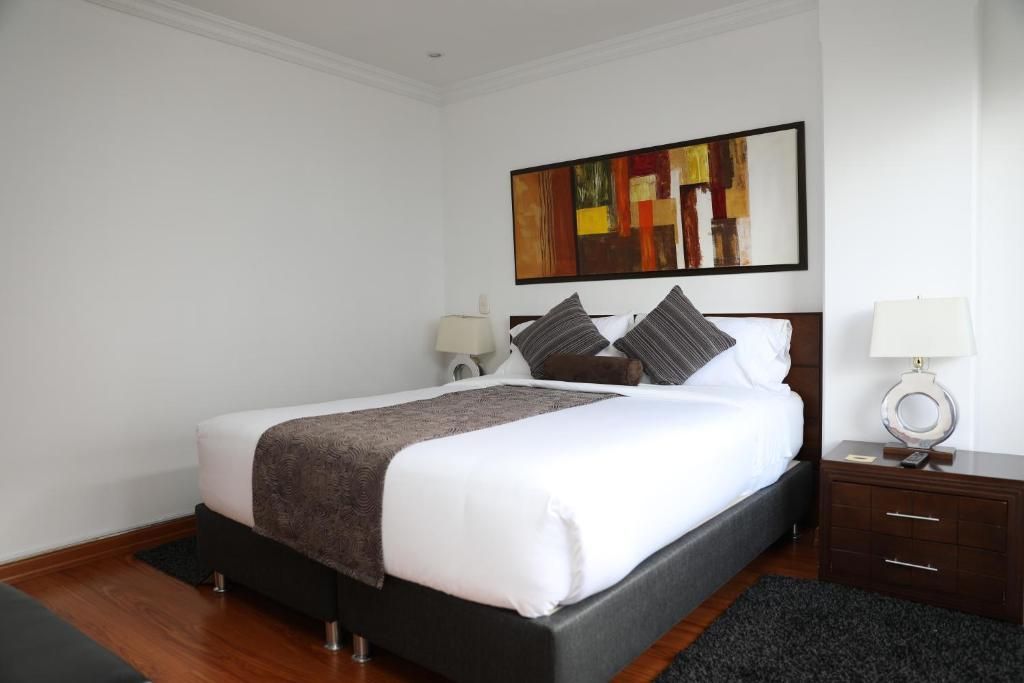Quarto de hotel com cama, mesas de cabeceira, um quadro na parede e um tapete.