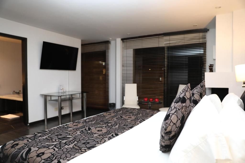 Habitación de hotel con cama, televisor montado en la pared, escritorio con silla y ventana con persianas.