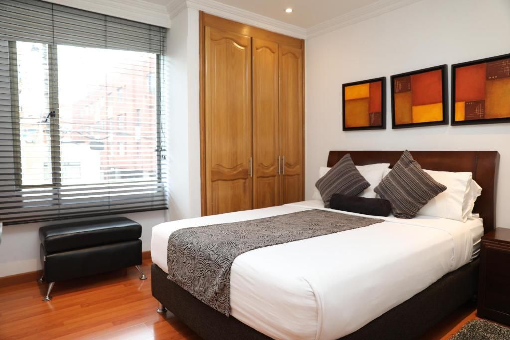 Ein Schlafzimmer mit einem Bett, einem Kleiderschrank, einer Bank und Kunstwerken an der Wand.