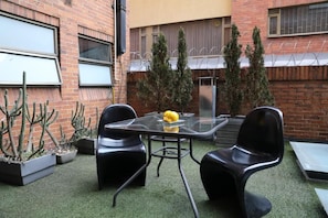An outdoor seating area with a glass table and chairs, surrounded by potted plants and a brick wall. - Hotel Suites 108 (Bogotá)