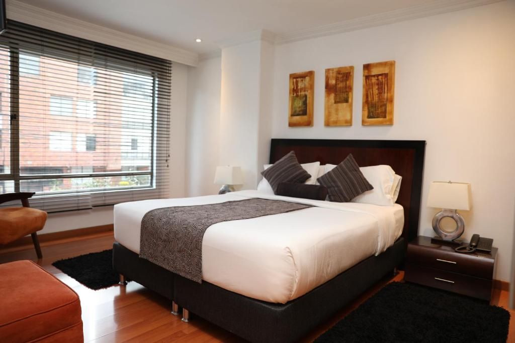 Una habitación de hotel con una cama grande, una mesita de noche, una silla y una obra de arte en la pared.