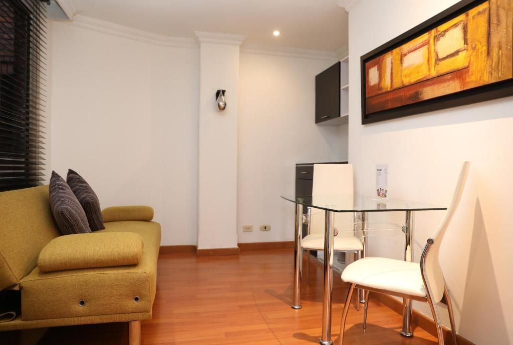 Una sala moderna con sofá, una mesa de comedor de cristal y un televisor montado en la pared.