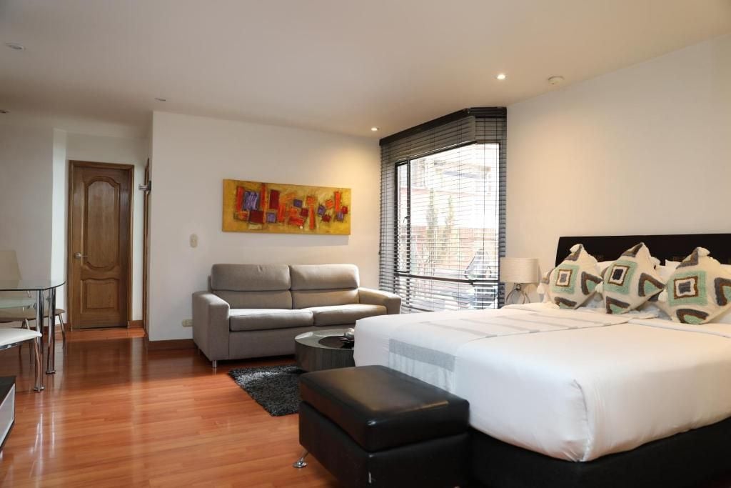 Ein modernes Schlafzimmer mit einem Bett, einem Sofa, einem Schreibtisch und einem Fenster mit Jalousien.
