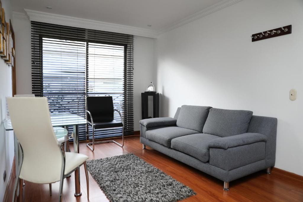 Ein Wohnzimmer mit einem grauen Sofa, einem weißen Sessel, einem Glastisch und einem schwarzen Schrank.