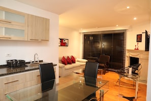 A modern kitchen with a glass dining table, a sofa with red cushions, and a fireplace. - Hotel Suites 108 (Bogotá)