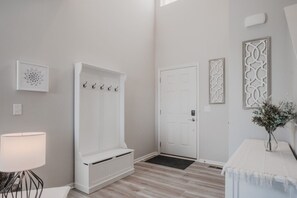 Ein Zimmer mit einer weißen Tür, einem Kleiderhaken, einem Heizkörper und einem kleinen Tisch mit einer Vase.