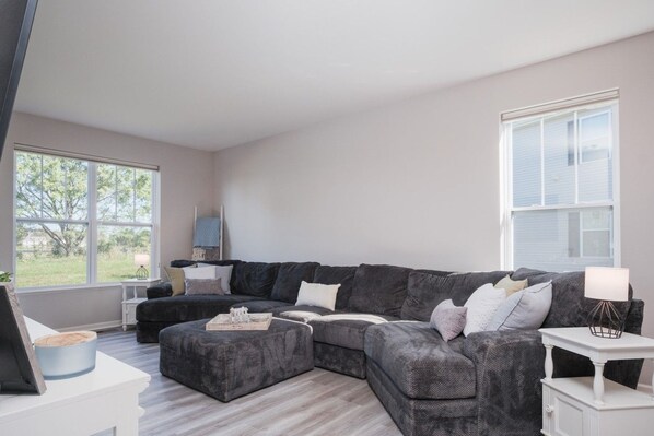A modern living room with a sectional sofa, a small side table, and a large window providing a view of the outdoors.