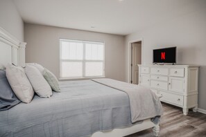 A bedroom with a bed, a dresser, a television, and a window.