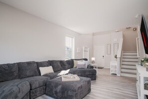 Ein modernes Wohnzimmer mit einer grauen Eckcouch, einem kleinen weißen Beistelltisch und einer Treppe, die zu einer oberen Etage führt.