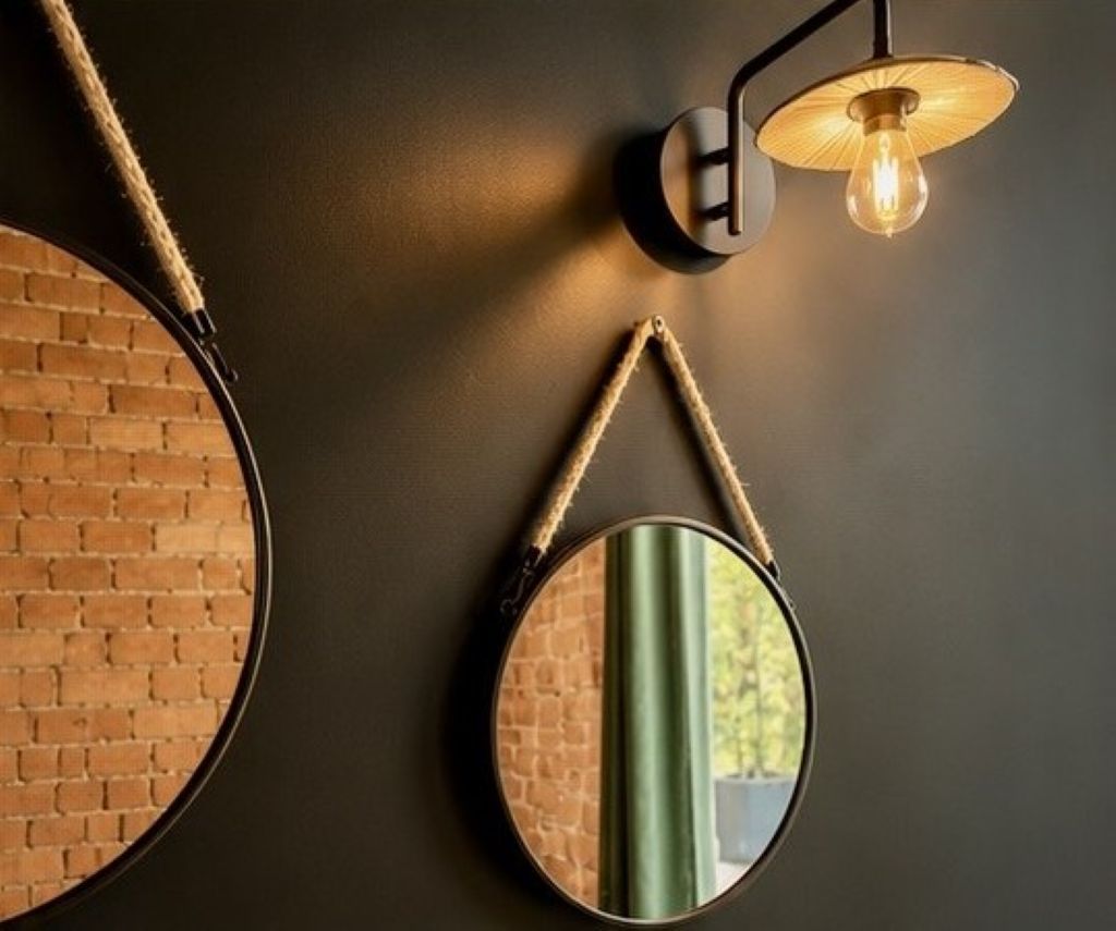 A wall-mounted mirror with a rope handle, a round mirror, and a wall sconce with a light bulb.