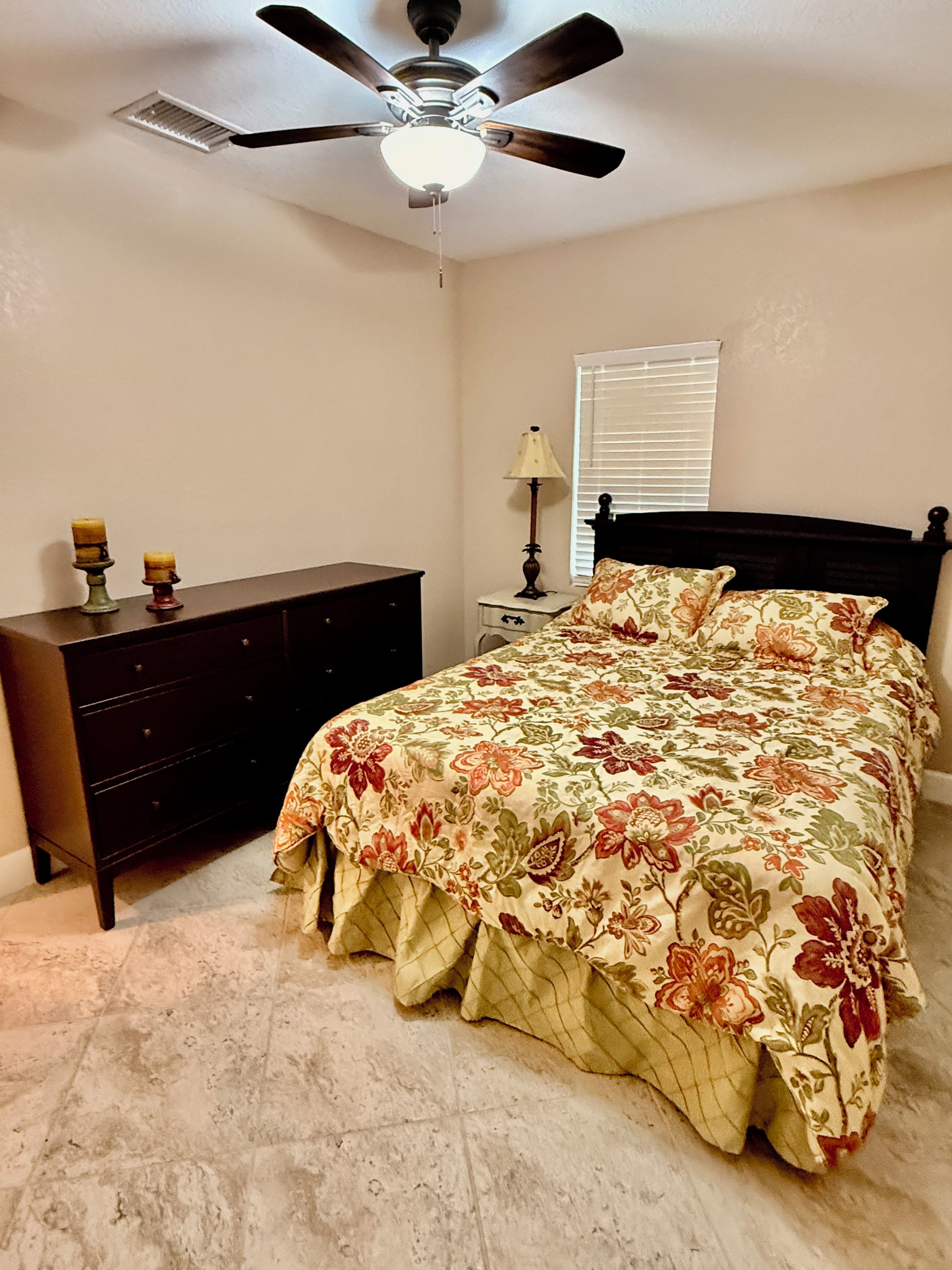 A bedroom with a bed, a dresser, a ceiling fan, and a window with blinds.