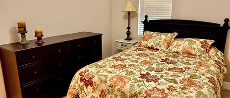A bedroom with a bed, a dresser, a ceiling fan, and a window with blinds.