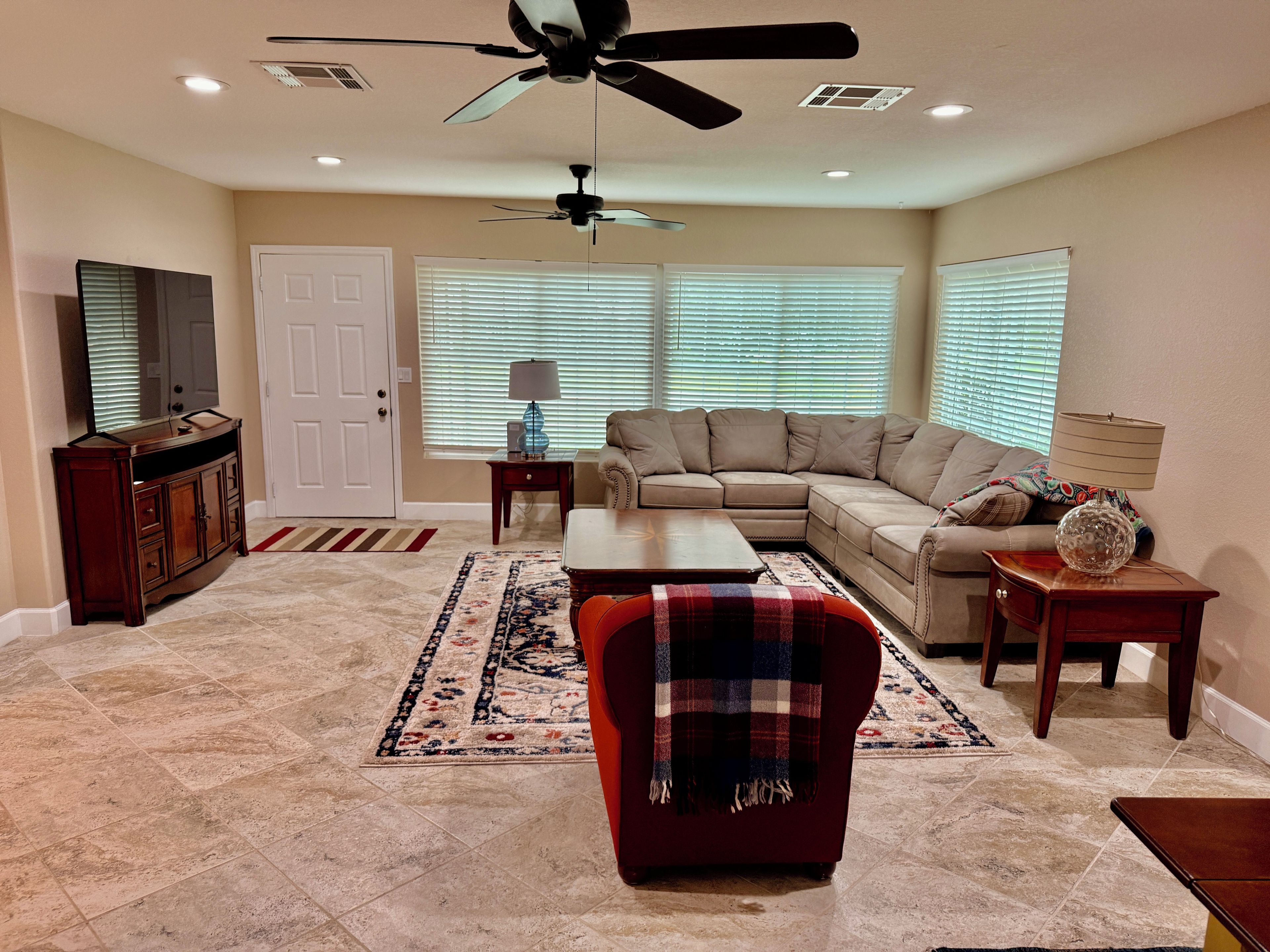 A living room with a sectional sofa, a red armchair, a coffee table, a TV, and a ceiling fan.