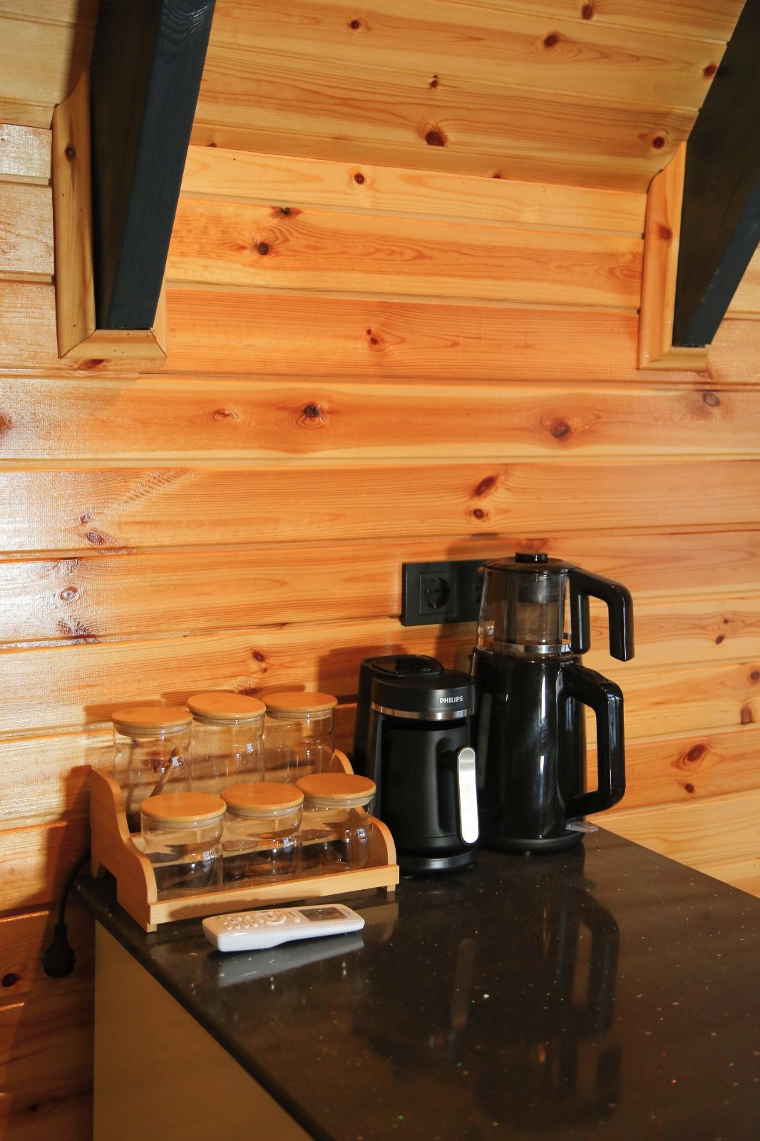 A kitchen with wooden walls, a coffee maker, a coffee pot, and a jar holder.