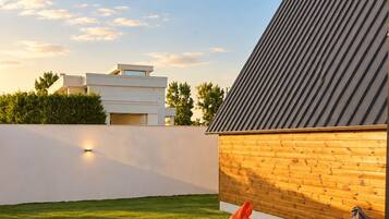 Un edificio moderno con techo inclinado y pared de madera. Tres sillones de saco en un césped.