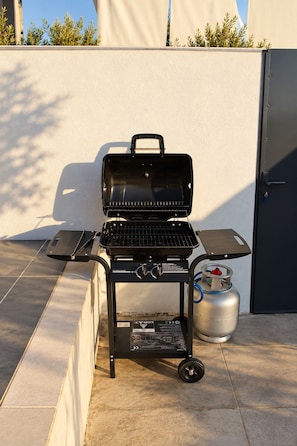 Una parrilla de gas portátil sobre ruedas, con un quemador lateral y tanque de propano.