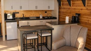 Una cocina moderna estilo loft con zona de comedor, que presenta un techo alto con vigas a la vista, un horno empotrado y una cafetera.