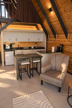 Una cocina moderna estilo loft con zona de comedor, que presenta un techo alto con vigas a la vista, un horno empotrado y una cafetera.