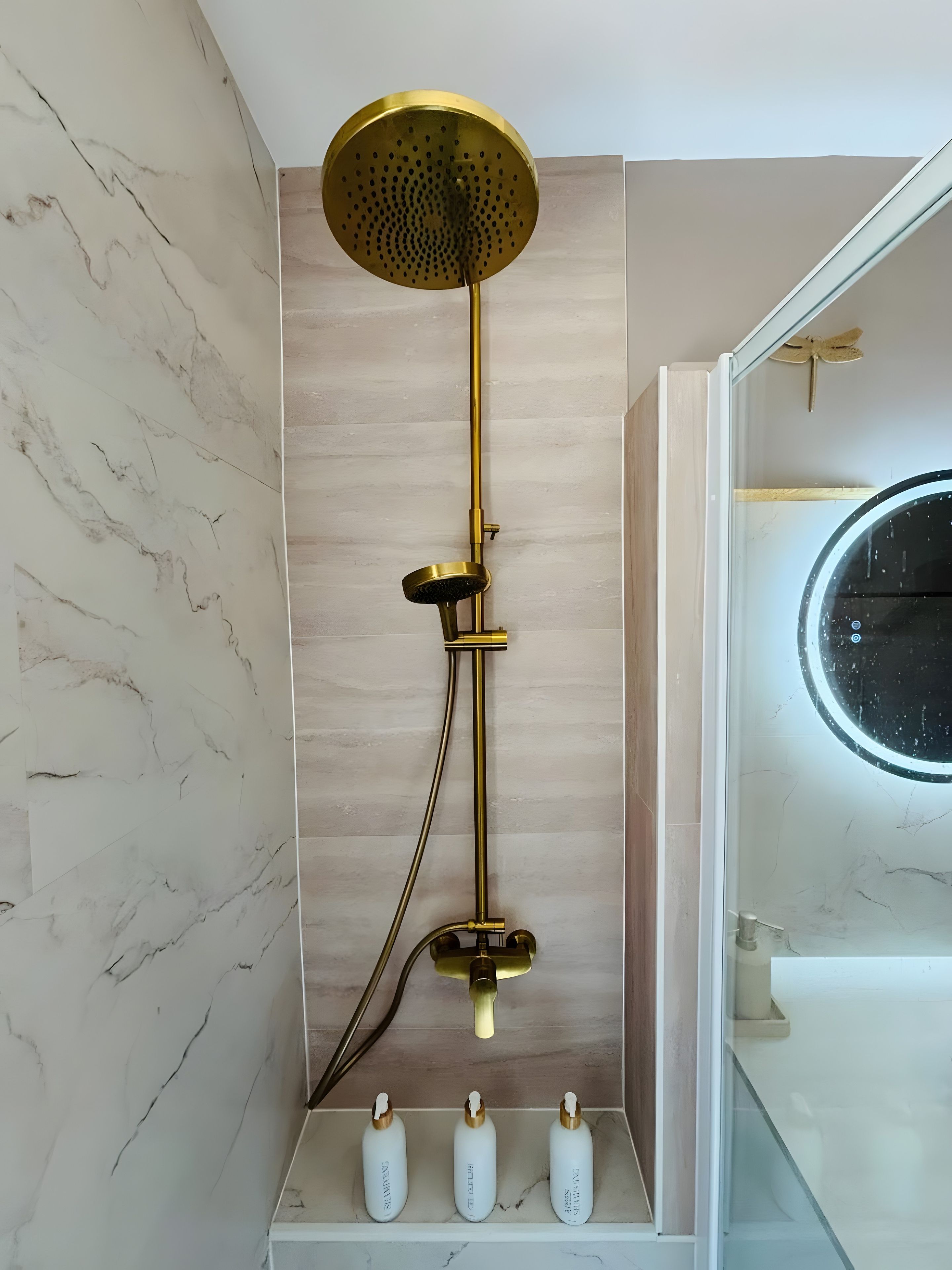 A modern bathroom with a gold showerhead, marble walls, and a glass-enclosed mirror.