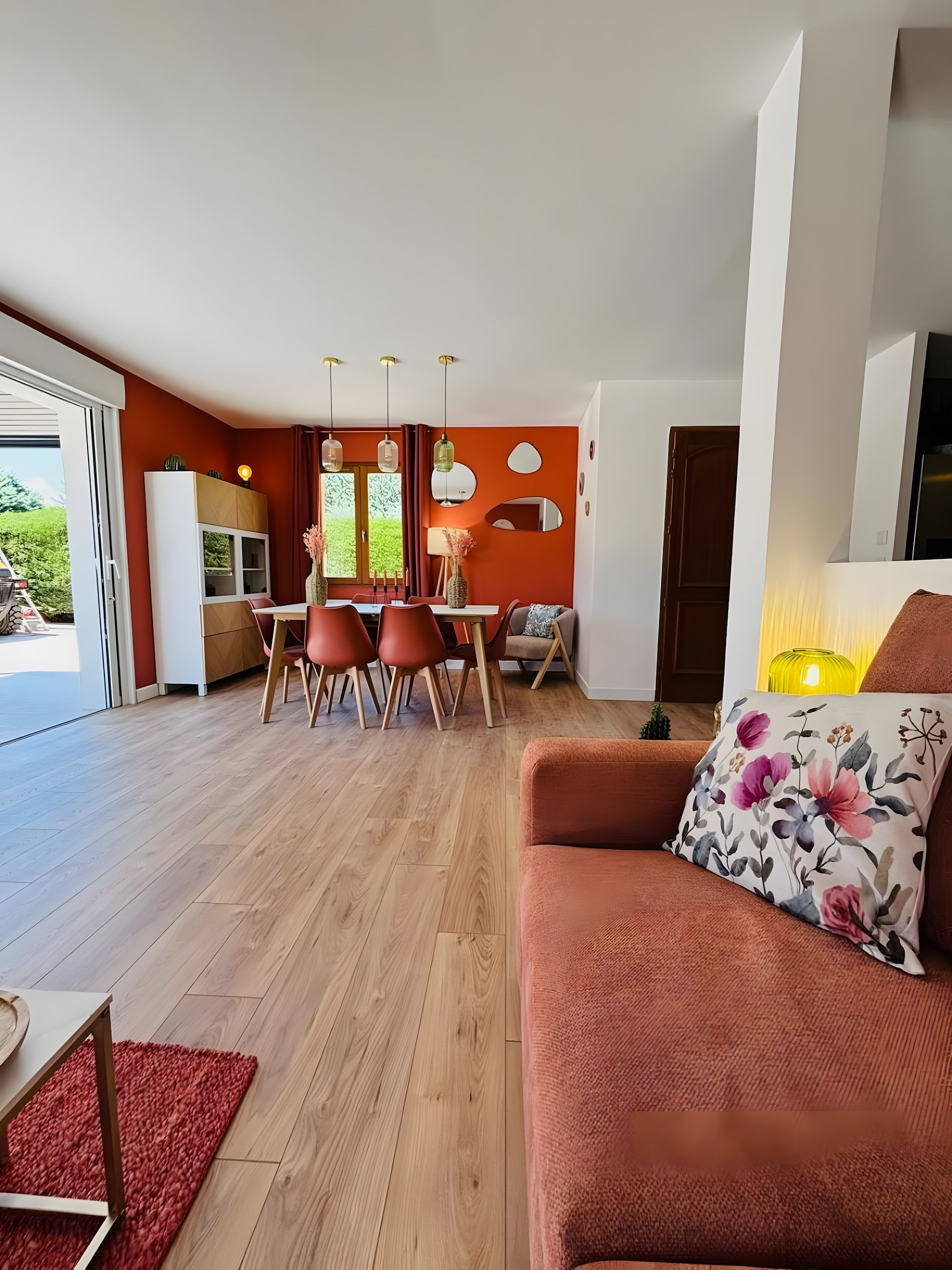 A modern living room with a sofa, a dining area with chairs, and a kitchen visible through an open door.