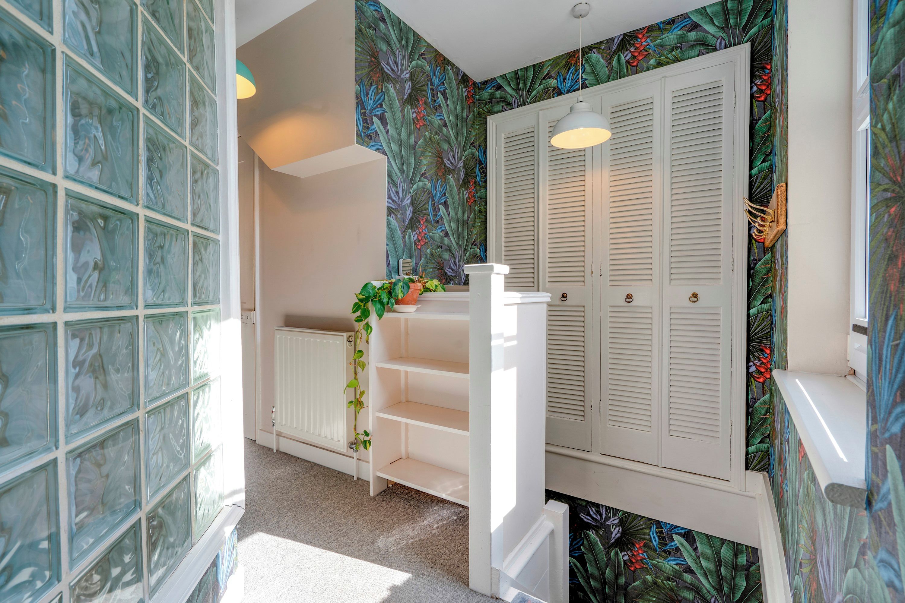 Une salle de bain avec une douche à parois de verre, un radiateur blanc, une étagère avec une plante et une porte dotée de volets à persiennes.