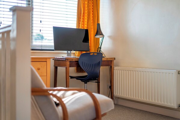 Een kamer met een houten bureau, een beeldscherm, een stoel, een lamp en een radiator.